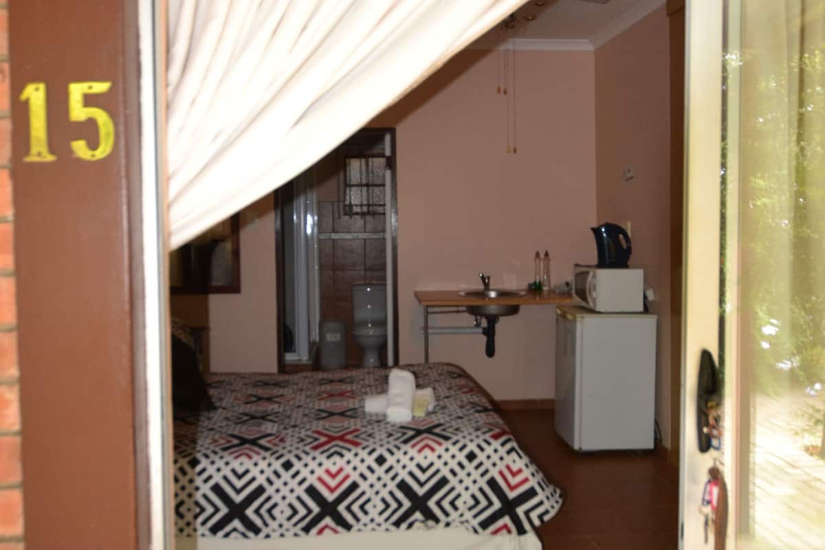 A room with a bed, a small kitchenette, and a door marked with the number 15.