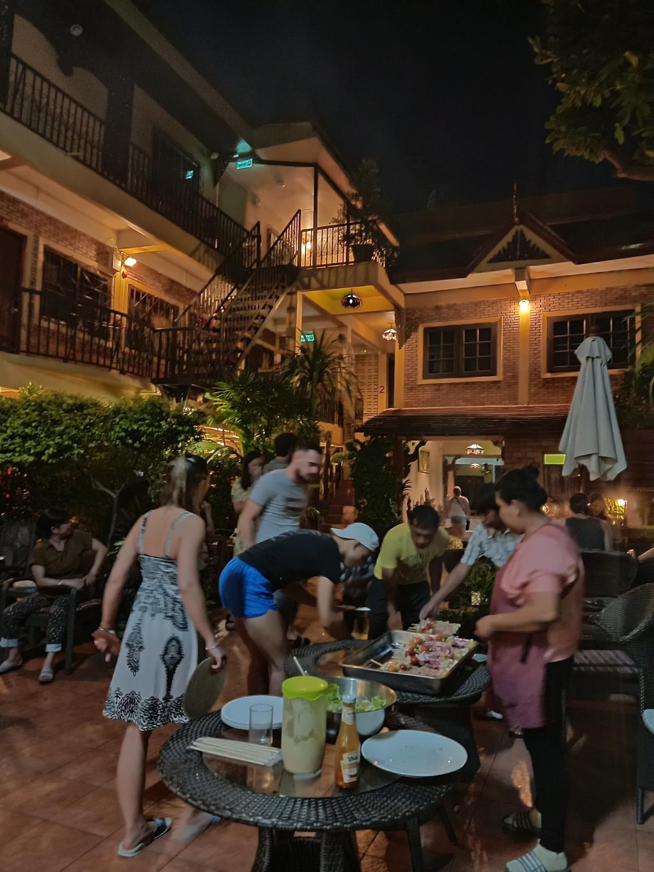 An outdoor dining area with tables and chairs, surrounded by buildings with balconies and railings.