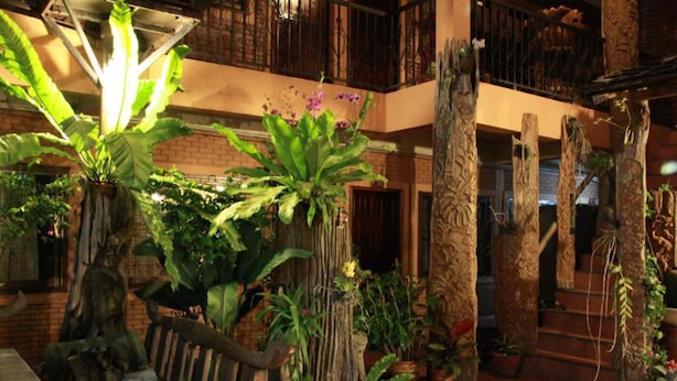 Un espacio interior amplio con un banco de madera, plantas en macetas y una escalera que conduce a un nivel superior.