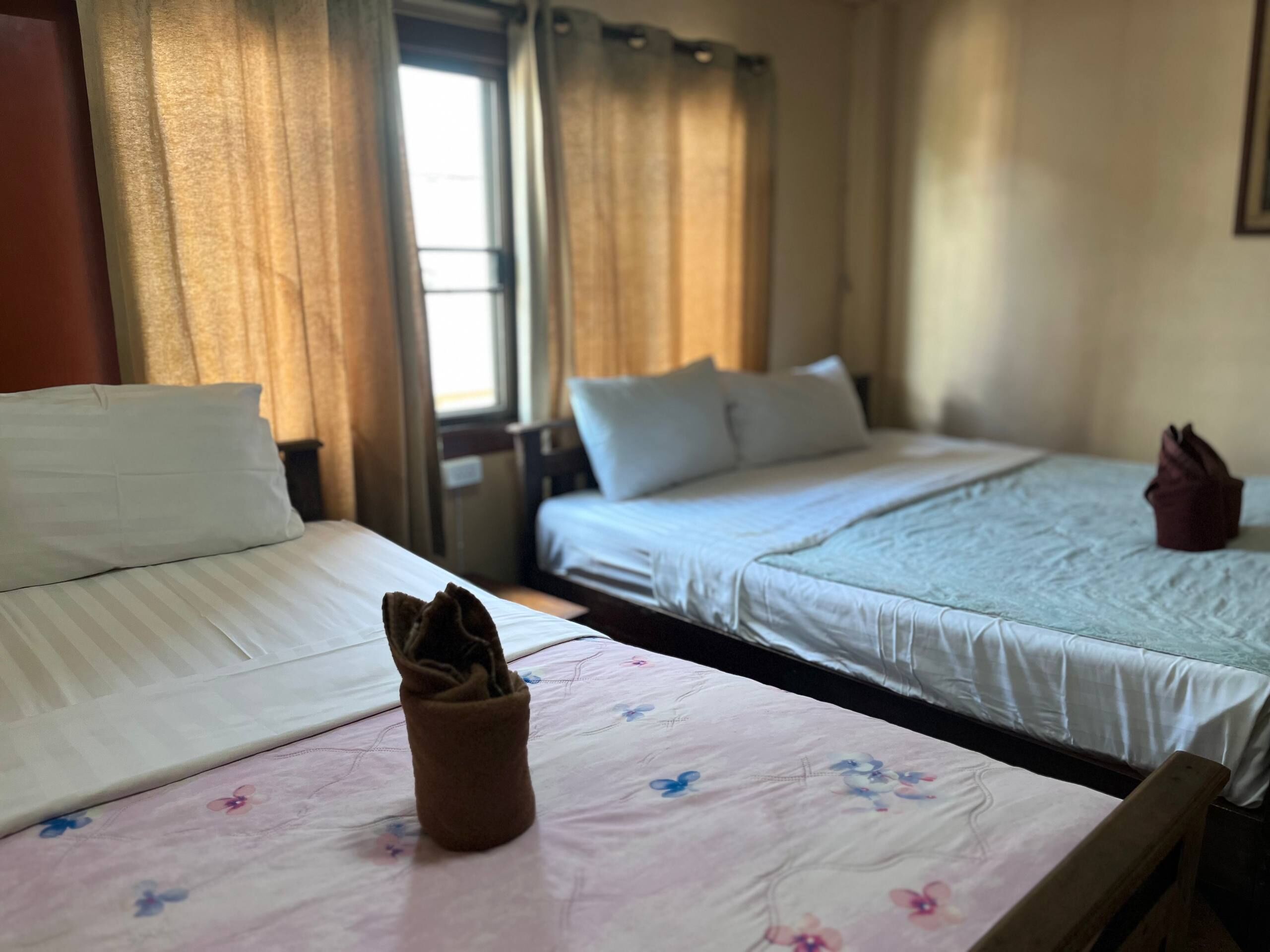 Habitación de hotel con dos camas, una ventana con cortinas y un cabecero de madera.