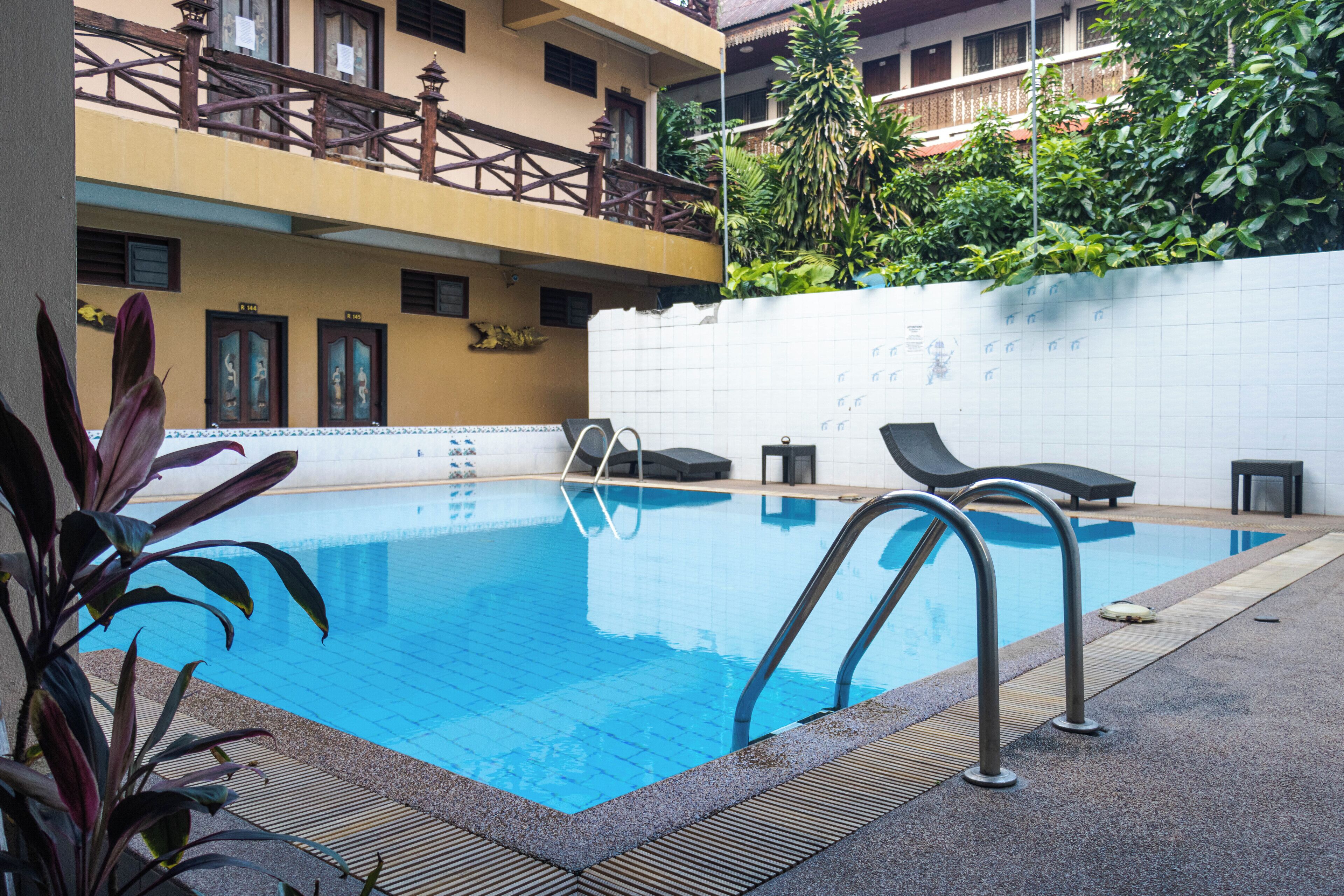 Une piscine avec des chaises longues, une terrasse carrelée et un bâtiment doté de balcons et de fenêtres en arrière-plan.