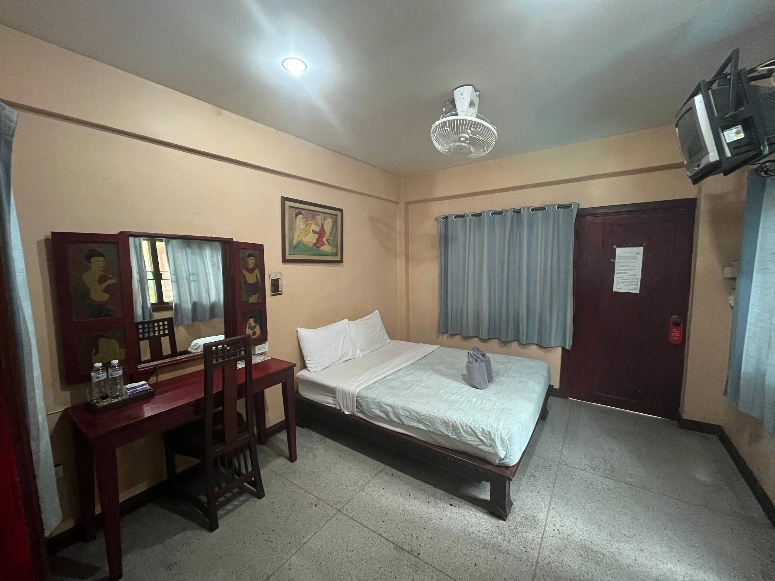 Una habitación de hotel con una cama, un escritorio, una silla, un ventilador de techo y un televisor.