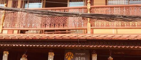 Un edificio de estilo arquitectónico tradicional, con un balcón que presenta barandillas intrincadas y un letrero para cajero automático Krungsri.
