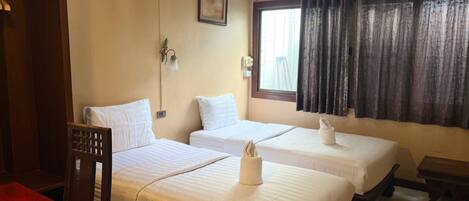 A hotel room with two beds, a wooden chair, a small table, a window with curtains, and an air conditioning unit.