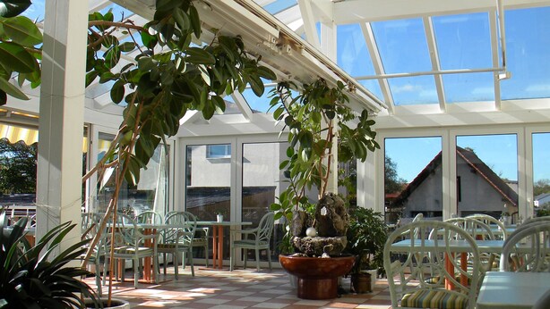A conservatory with a checkered floor, potted plants, and white furniture. - Hotel Landgasthof Nagerl (Marzling)