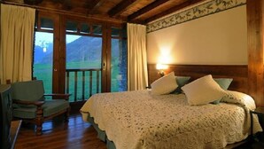 Um quarto aconchegante com uma cama grande, vigas de madeira, vista para o exterior e uma cadeira perto da janela.