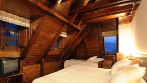 Quarto de cabana de madeira com uma cama, uma televisão e uma janela com cortinas.