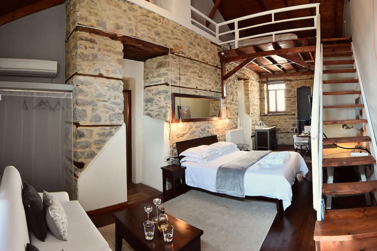 Un dormitorio con pared de piedra, escalera de madera, cama, mesita de noche y televisor.