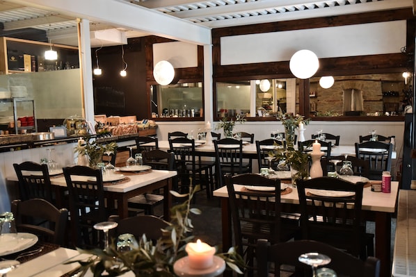 A restaurant interior with wooden tables and chairs, candle centerpieces, and hanging pendant lights.