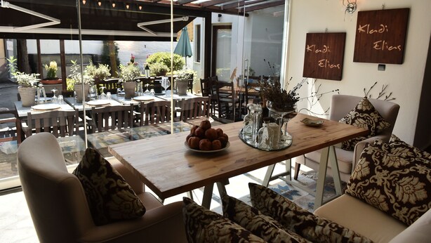 A cozy dining area with a wooden table, chairs, and a sofa. There are potted plants and a glass partition. - Culinary Boutique Hotel Kladi Elias (Pangaio)