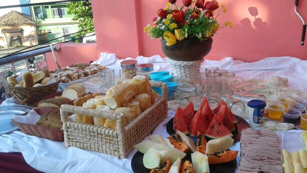 Una mesa de buffet con diversos alimentos y bebidas, incluyendo pan, frutas y una decoración floral.