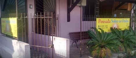A building with a yellow signboard, a metal gate, and potted plants.