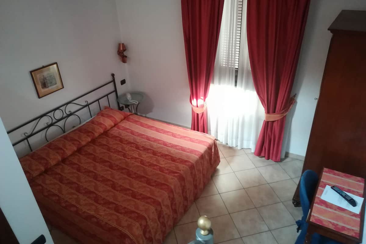 Een slaapkamer met een bed, een bureau, een stoel, een telefoon en een raam met gordijnen.