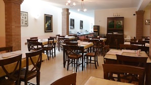Un restaurante con varias mesas y sillas de madera, pilares de ladrillo y lámparas colgantes.