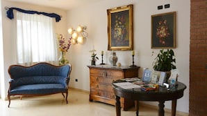 Una sala de estar con un sofá azul, un aparador de madera, una mesa redonda con papeles y dos cuadros enmarcados en la pared.