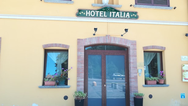 Un edificio con un letrero que dice "HOTEL ITALIA" sobre la entrada. Hay dos macetas con plantas a cada lado de la puerta.