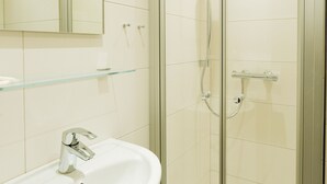 Un baño con ducha de vidrio, lavabo blanco y espejo sobre el lavabo.