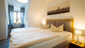 Una cama bien hecha con cabecera, una lámpara de noche y una ventana con cortinas.