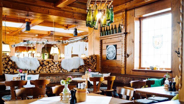 Un interior rústico de madera con mesas y sillas de madera, lámparas colgantes y un ventanal con vistas.