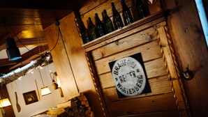 Un interior rústico con paredes de madera, una chimenea de piedra y una estantería con botellas.