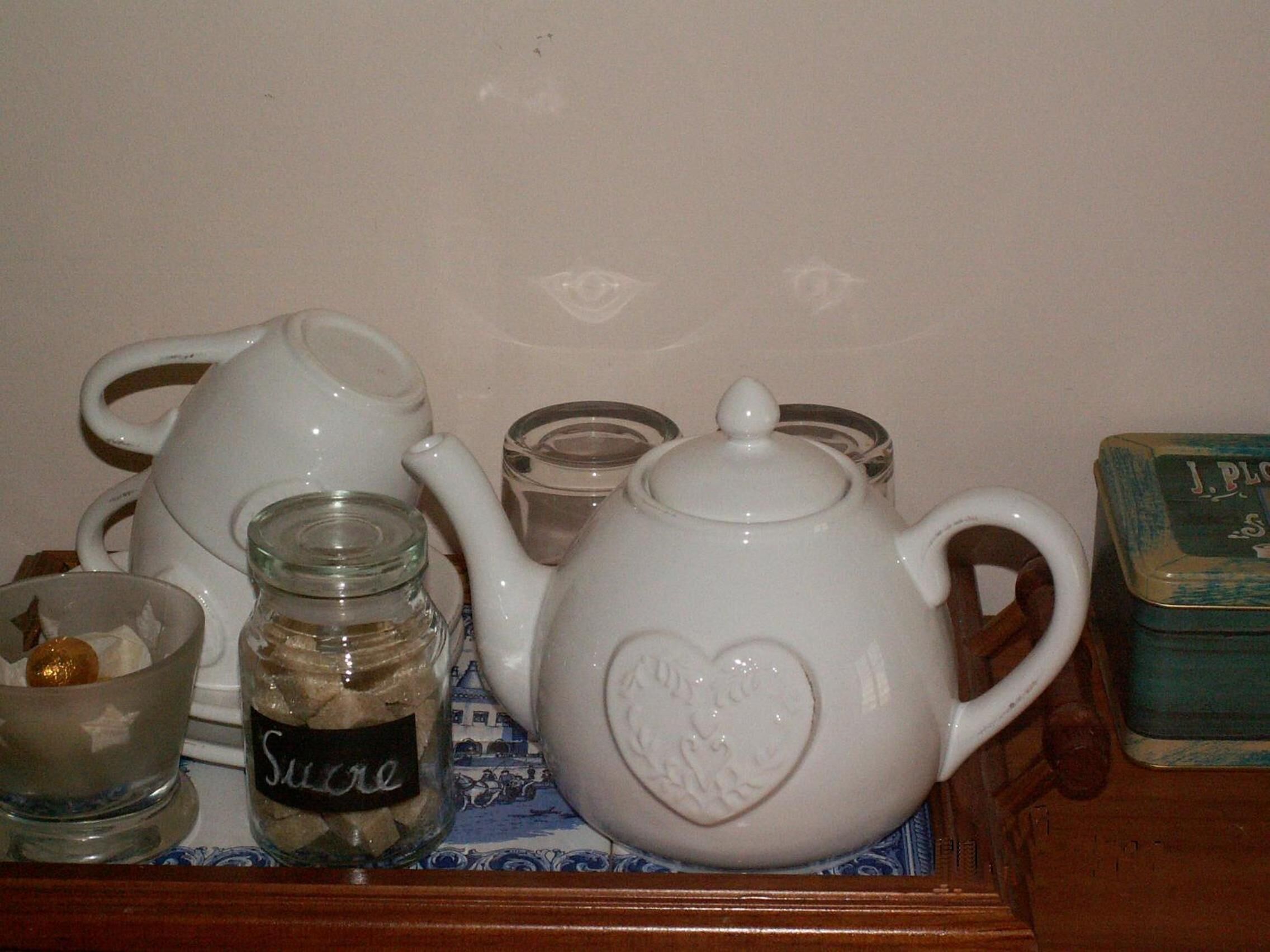 A white teapot with a heart design, a glass jar labeled "Suckle," a glass cup, and a small container on a table.
