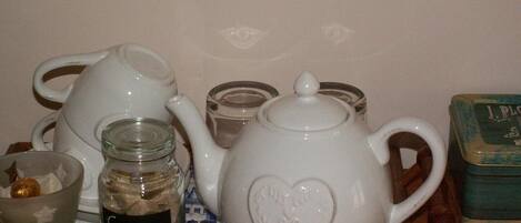 A white teapot with a heart design, a glass jar labeled "Suckle," a glass cup, and a small container on a table.