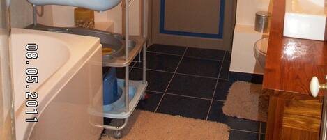 A bathroom with a white bathtub, a wooden door, and a framed picture on the wall.
