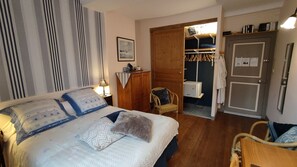 A bedroom with a bed, bedside lamps, a wardrobe, a chair, and a door leading to a bathroom. - Dodo et tartines B&B (Bayeux)