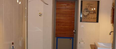Une salle de bain avec une baignoire, des toilettes et un lavabo. On y trouve une porte en bois avec un cadre bleu, une citation encadrée au mur et une petite décoration représentant un phare sur le bord de la baignoire.
