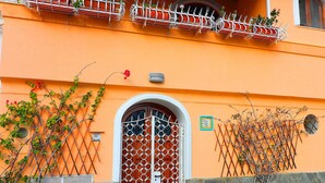A building with a red door, a balcony with plants, and a stone wall. - Angolo di Paradiso (Positano)