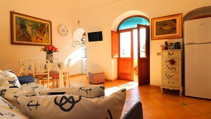 A cozy living room with a sofa, a dining table, and chairs. There is a painting on the wall, a television, and a refrigerator. - Angolo di Paradiso (Positano)