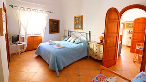 A bedroom with a bed, a desk, a chair, a wardrobe, and a door leading to another room. - Angolo di Paradiso (Positano)