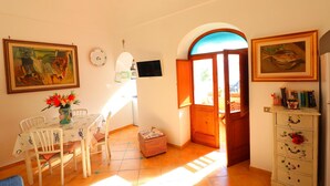 A dining area with a table, chairs, a vase with flowers, and a television on the wall. - Angolo di Paradiso (Positano)