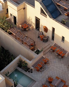 Una terraza en la azotea con varias zonas de estar, una piscina y vistas de los edificios circundantes.