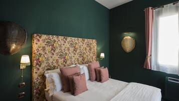 Een net opgemaakt bed met witte en roze beddengoed, een bloemen hoofdbord en wandlampen.