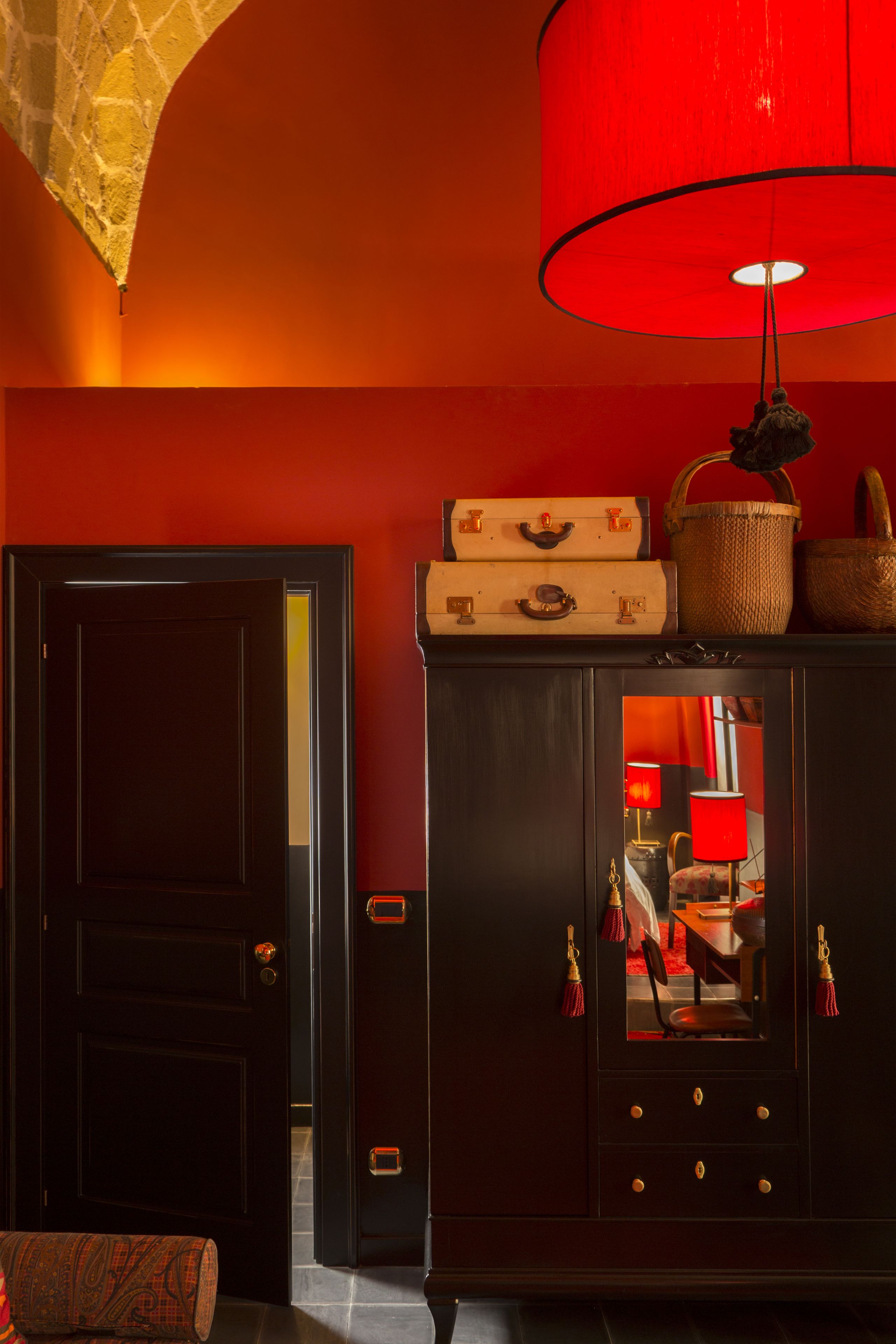 Ein dunkles Holzschränkchen mit einer roten Lampe, einem Spiegel und alten Koffer.