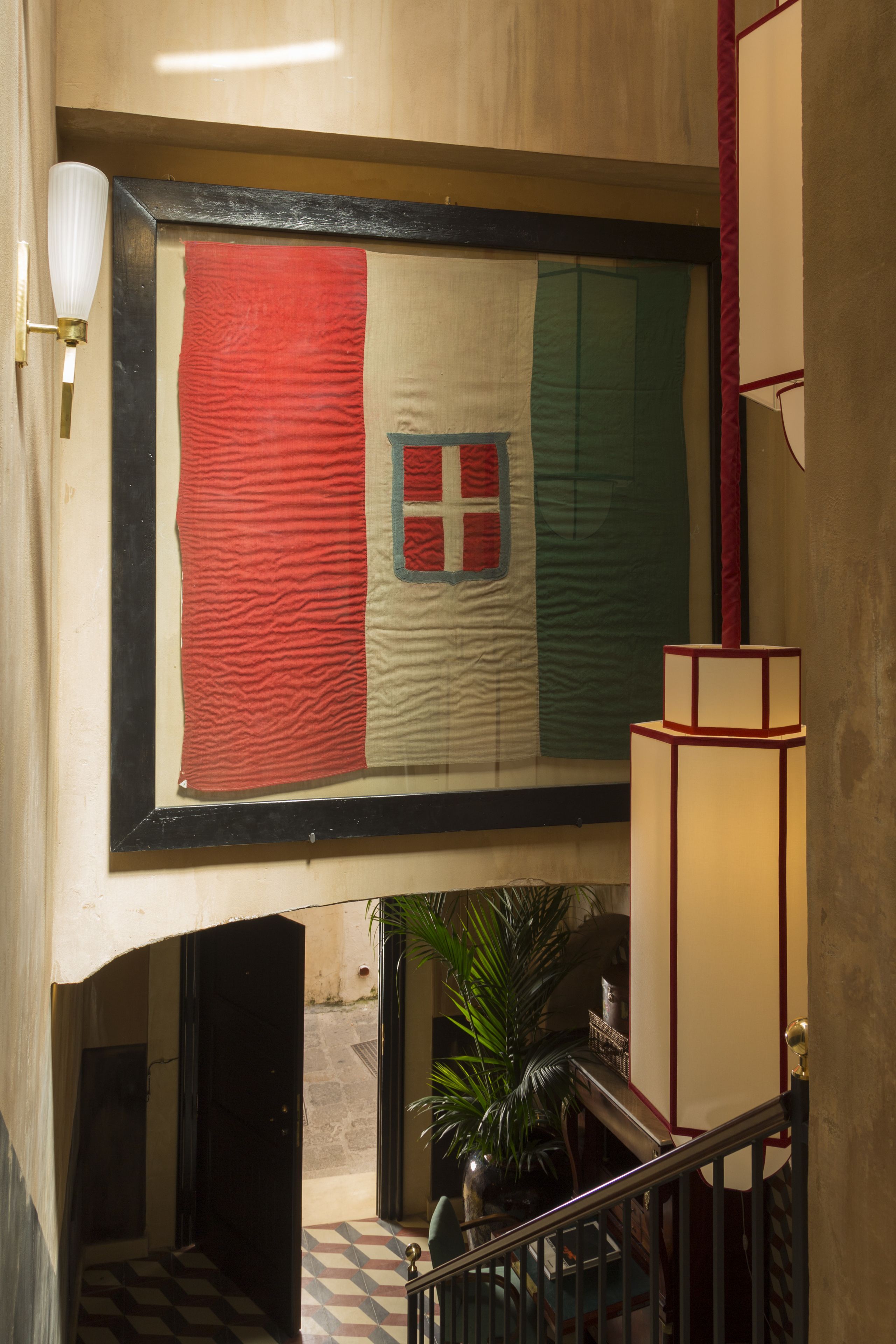 A framed flag with a red, white, and green design, a staircase with a checkered floor, and a potted plant.