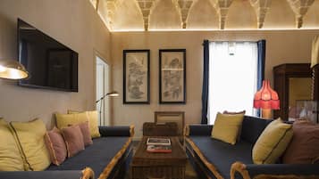 Una sala de estar acogedora con un sofá azul oscuro, cojines amarillos y marrones, una mesa de centro de mimbre con libros y obras de arte enmarcadas en las paredes.
