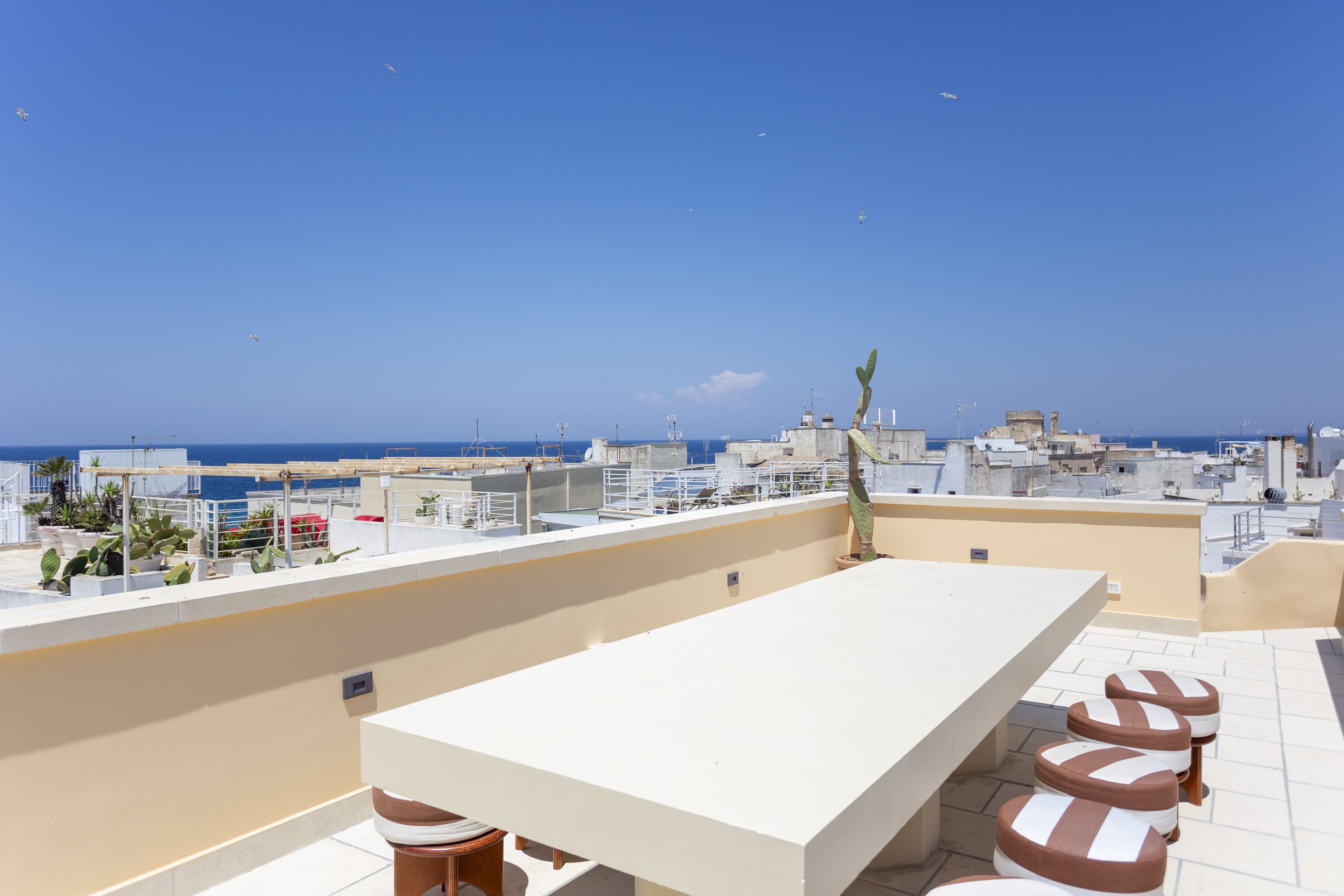 Terraza en la azotea con una mesa larga y sillas, con vista a una ciudad costera.