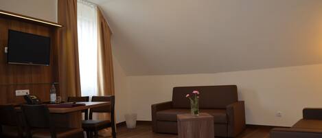 A modern living room with a flat-screen TV, a sofa, a coffee table, and a dining area with chairs and a table.