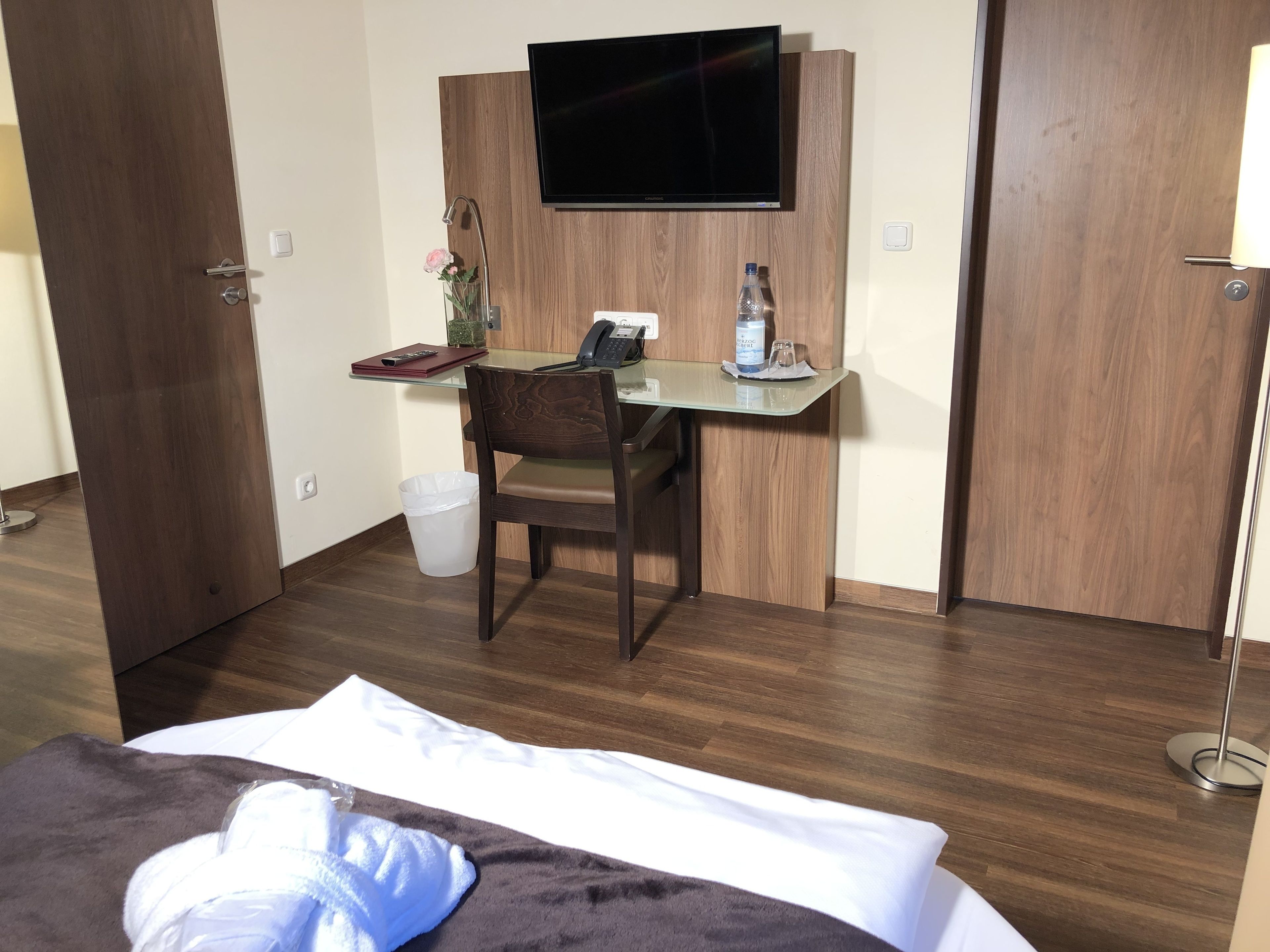 Hotellihuone, jossa on sänky, työpöytä tuolilla, televisio ja roskakori.