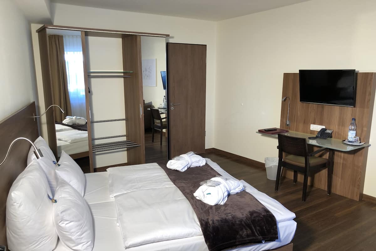 Una habitación de hotel con una cama, un escritorio, un televisor y un espejo.