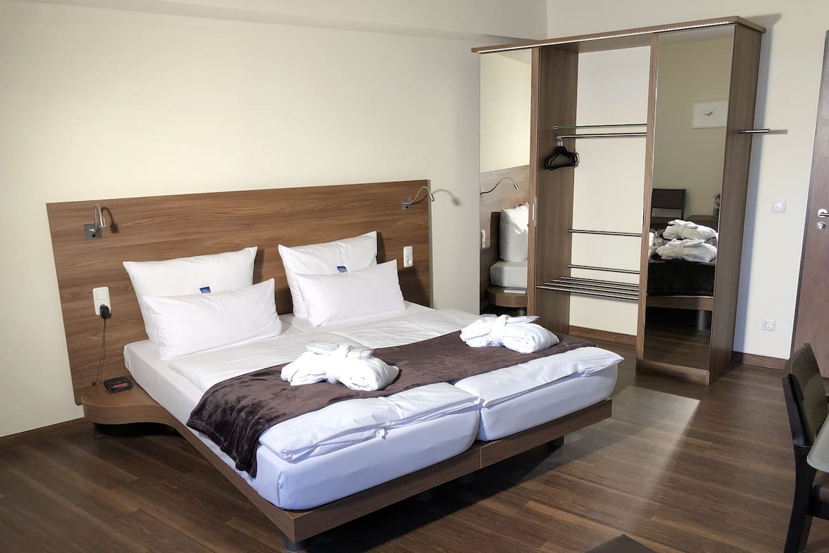 Una cama bien hecha con sábanas y toallas blancas, un cabecero de madera y una mesita de noche con una lámpara.