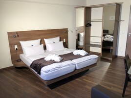A neatly made bed with white linens and towels, a wooden headboard, and a bedside table with a lamp.