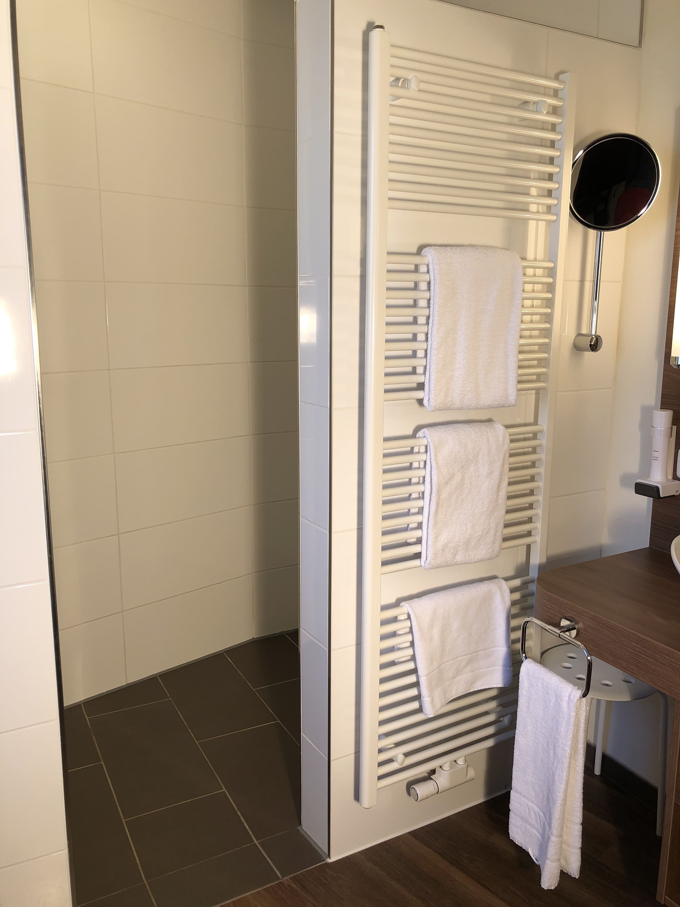 A bathroom with a white towel rack holding three towels, a mirror, and a wooden vanity with a sink.