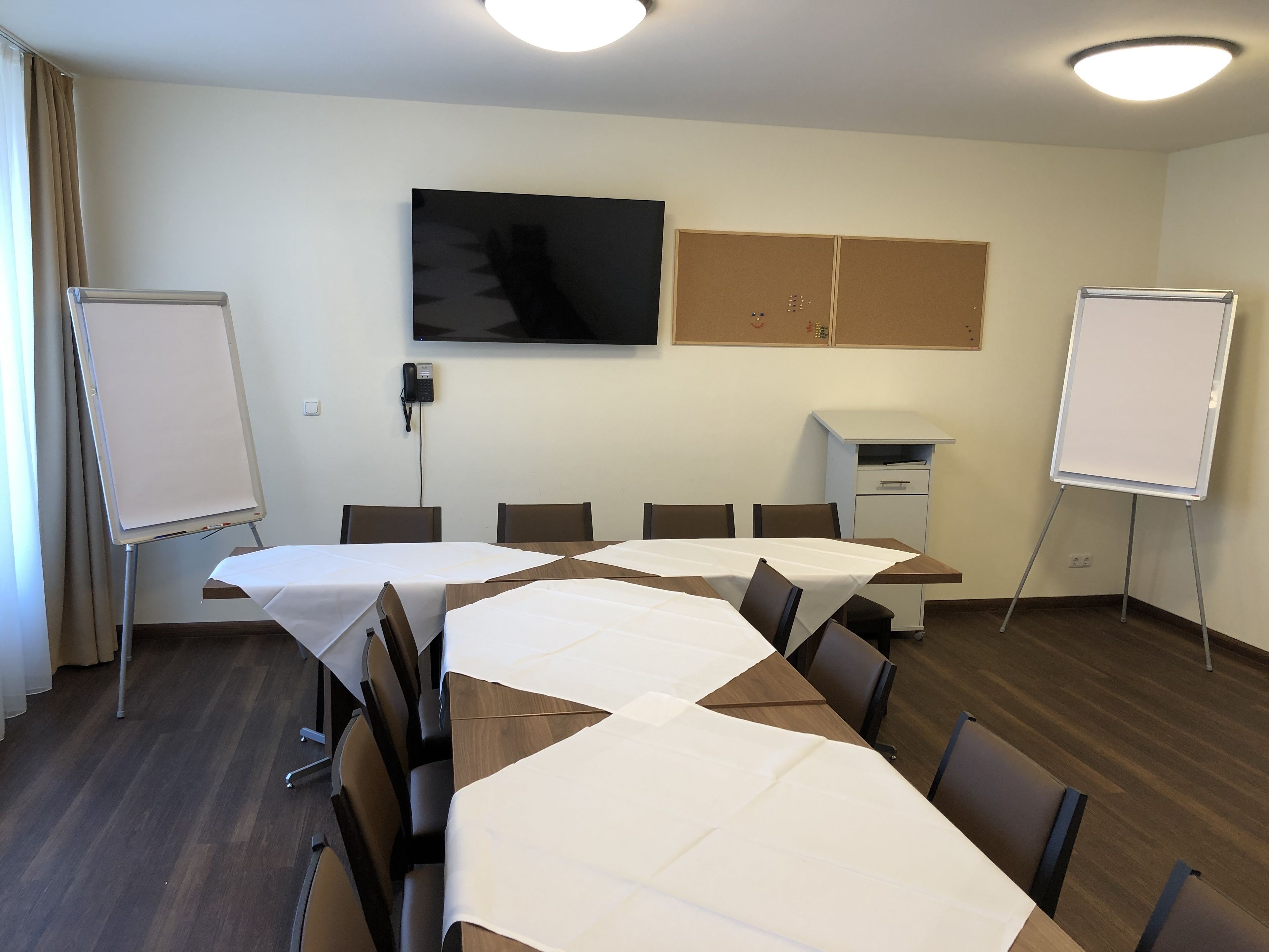 Een vergaderruimte met een lange tafel, stoelen, een whiteboard, een televisie en een telefoon aan de muur.
