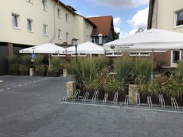 A courtyard with outdoor seating under white umbrellas, a parking sign, and a building with a brick facade and multiple windows.