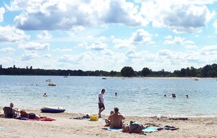 A beach with people swimming and sunbathing, boats on the water, and a clear sky.