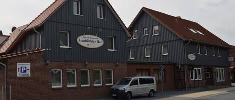 A hotel named Isenbütteler Hof with a parking sign and a van parked in front.