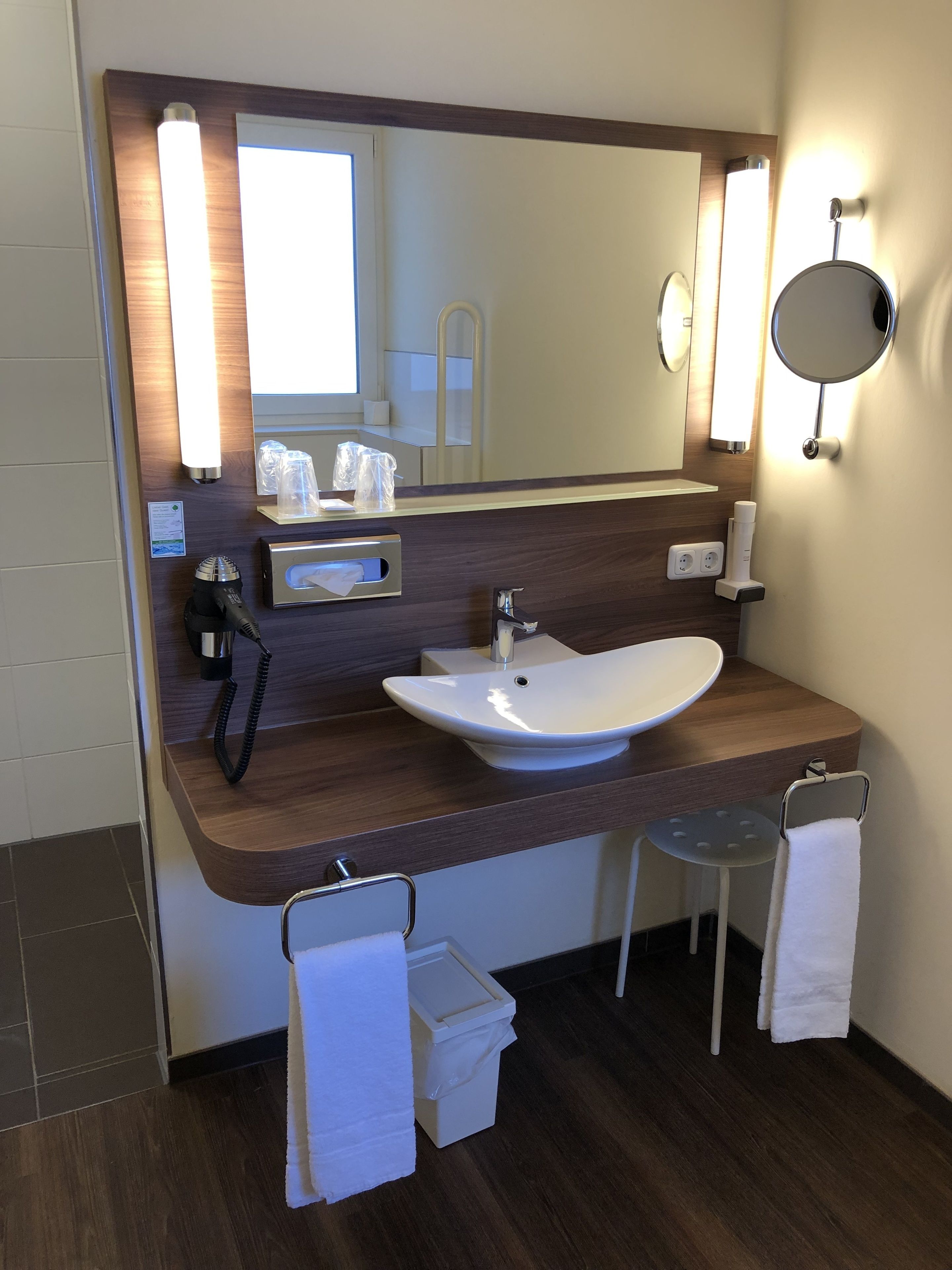 A modern bathroom with a wooden vanity, a large mirror, and a white sink.